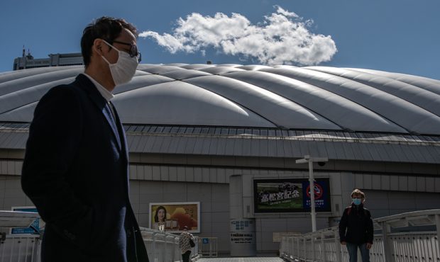 People wearing face masks walk past Tokyo Dome where a number of events including pop concerts have...