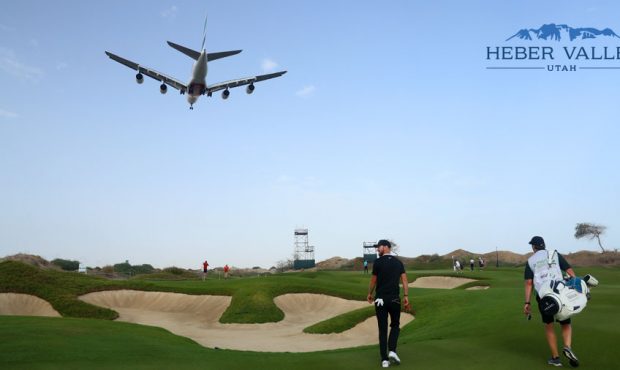 Chris Wood of England and his caddie walk along the 14th hole as a airplane passes overhead during ...
