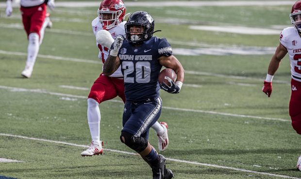 Jaylen Warren #20 of the Utah State Aggies rushes the ball past Deonte Perry #17 and Evan Williams ...
